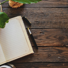 Notebook and coffee, flowerpot, notebook and pen, wooden background, top view. Work at home. Office accessories and office wooden table.