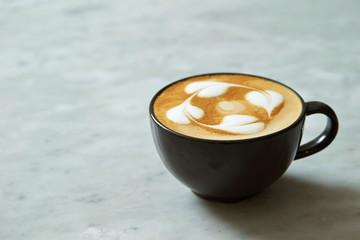 Latte in black cup on stone background 