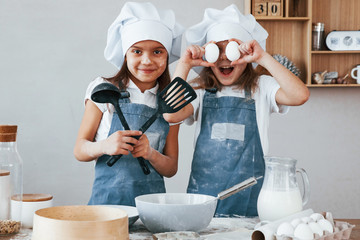 Two little girls in blue chef uniform have fun while preparing food on the kitchen