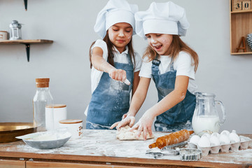 Two little girls in blue chef uniform kneading dough on the kitchen