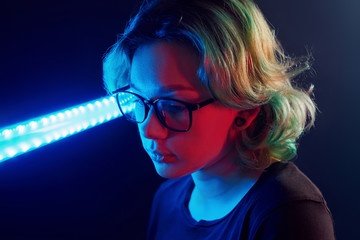 Portrait of young alternative girl in glasses with green hair in red and blue neon light in studio