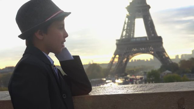 Handsome teenage boy in a hat is talking on the phone and watching on the Eiffel tower, Paris, France