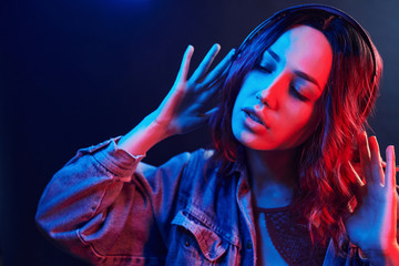Portrait of young girl that listening to music in headphones in red and blue neon in studio