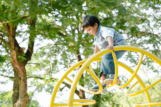 Asian Little Boy Climbs Down The Curve Frame On The Playground.