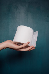 Female hand holds a roll of white toilet paper on a blue background