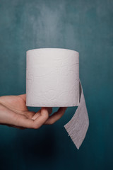 Female hand holds a roll of white toilet paper on a blue background