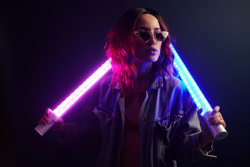 Portrait of young girl in glasses holding light sticks in red and blue neon in studio - obrazy, fototapety, plakaty