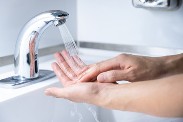 Man washing hands 7 step with soap or sanitizer gel on sinks faucet with water for clean virus and bacteria, health care concept (select focus)
