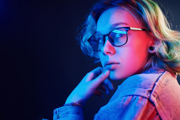Portrait of young alternative girl in glasses with green hair in red and blue neon light in studio