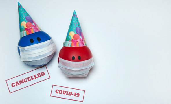 The concept of canceling celebrations due to the Covid-19 coronavirus pandemic. Balloons in party caps and medical masks, signs warning of quarantine on a white background. Free space.