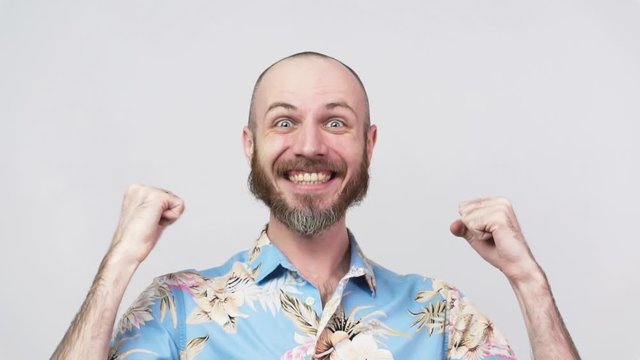 Happy man wearing hawaiian shirt celebrating a victory over white background, slow motion. Emotions of success, triumph, victory, winning and celebration.
