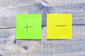 Two post its on wooden background with a plus and minus symbol