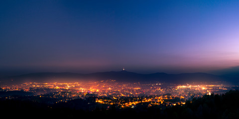 Shining town during dusk in the valley. Light fog flows above the town and disperse lights.