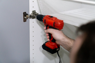 Man wotking with an electrical drilling machone. Mounting furniture in a new house or apartment as...
