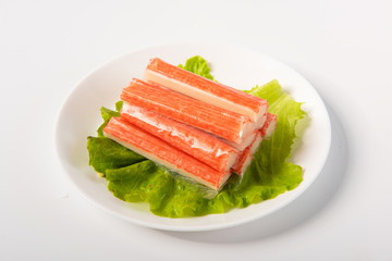 Crab sticks made of crab meat are placed on lettuce leaves, in delicate plates, isolated in white background