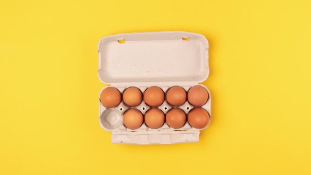 Eggs in a cardboard tray moves from the bottom, then disappear and appear in a box on a yellow background. Top view, stop motion animation