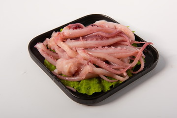 The fresh octopus is placed on the lettuce leaf, and it is placed on a black plate. On a white background, it is used as a kind of food for hotpot