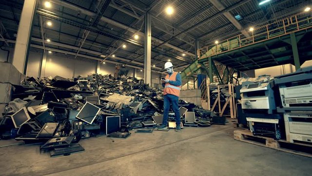 Recycling industry, used electronic recycling factory. Landfill worker with a smartphone near a pile of debris
