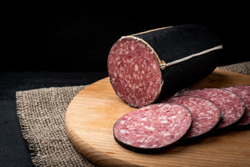 Smoked black-coated sausage salami on black background.