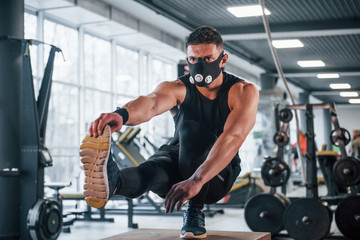 Fototapeta na wymiar Strong young man in sportive clothes and scary mask doing push ups on one leg in gym