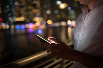 Close-up of male hands using smartphone at night on city shopping street. Searching or social networks concept