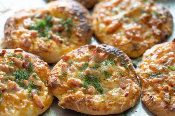 Homemade mini pizzas baked stuffed with cheese ham and greens on a baking sheet.