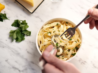 male hands eating pasta with parsley with fork and spoon