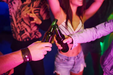 Celebrating and knocking bottles with alcohol. Young people is having fun in night club with...