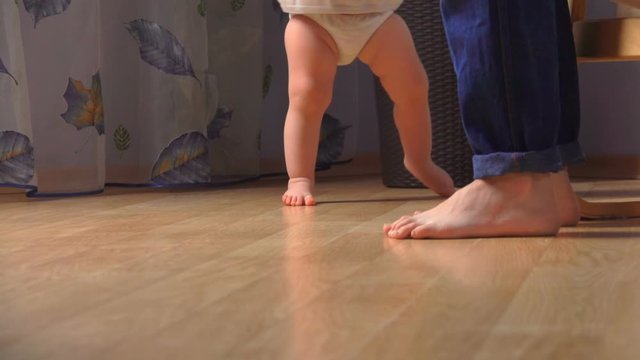 Mother is helping her little adorable baby to take the first steps. Low-angle feet view
