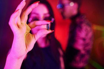 Close up view of woman's hands with drug pill. Young people is having fun in night club with...