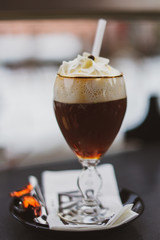 Closeup of delicious glass of Irish Coffee with heavy cream on top. High aperture, ski resort in the background. St Anton am Arlberg ski resort, Austria, Europe -Image