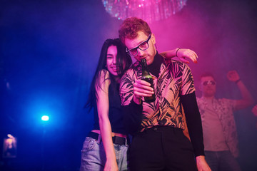Guy in glasses drinks beer. Young people is having fun in night club with colorful laser lights