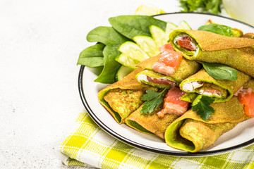 Green pancakes from spinach wrapped with salmon and cream cheese.