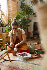 Young florist sitting on the floor and she is planting plants in the pots in the room