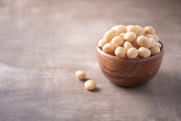 Macadamia nuts in wooden bowl on wood textured background. Copy space. Superfood, vegan, vegetarian food concept. Macro of macadamia nut texture, selective focus. Healthy snack. - obrazy, fototapety, plakaty