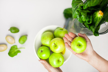 Girl takes a green apple from the table. On the table is a plate of apples and greens. Fresh,...