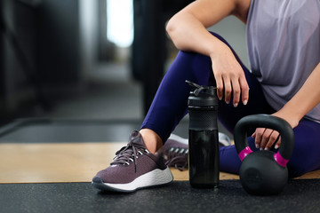 Fototapeta na wymiar The concept of the gym sport. Fitness equipment. A woman sits on the floor in sneakers. A kettlebell and dumbbells.