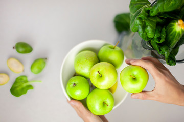 Girl takes a green apple from the table. On the table is a plate of apples and greens. Fresh,...