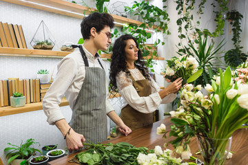 Obraz premium Attractive young male florist with glasses and apron is training at a flower shop