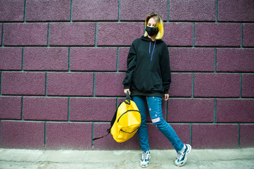 Teenager with yellow hair and backpack stand in front of brick wall