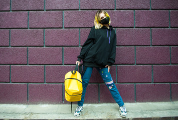 Teenager with yellow hair and backpack stand in front of brick wall