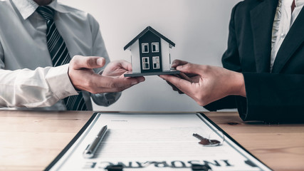 Agent is advising clients about home insurance contract agreements with house model in the office.