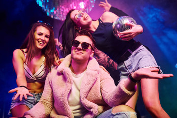 Elegant man in sunglasses in the midle feels like a boss. Young people is having fun in night club with colorful laser lights