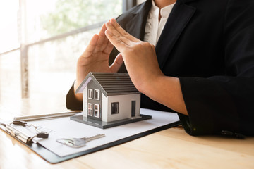 Agent is protecting a house model for present about home insurance in the office.