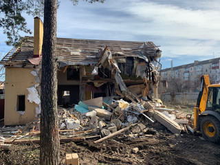 Fototapeta premium Ruined, brick, residential building. The ruins of a collapsed mansion in the forest. Demolition of an old house with an excavator. The destroyed walls of the building.