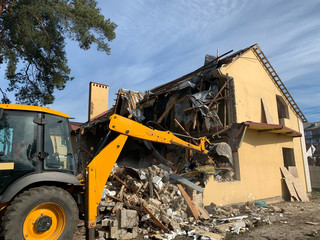 Ruined, brick, residential building. The ruins of a collapsed mansion in the forest. Demolition of an old house with an excavator. The destroyed walls of the building.