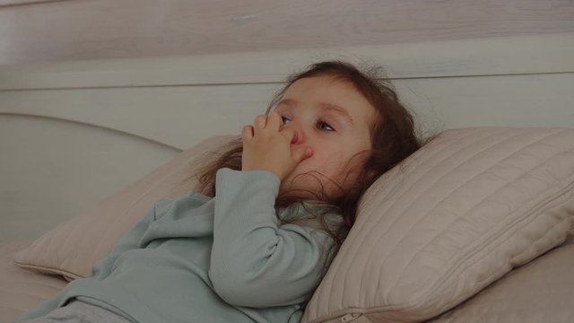 Thoughtful child picking nose. Serious little girl laying on bed. Feeling sleepy and tired.