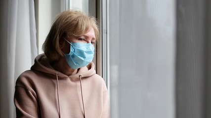 Sad senior woman with medical mask near the window