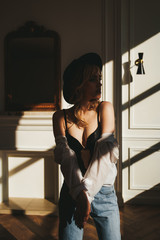 The concept of shooting in a photo Studio with hard lighting from the Windows. Sexy sensual blonde in a black hat , underwear and jeans poses for the camera in the shade on the floor of an apartment