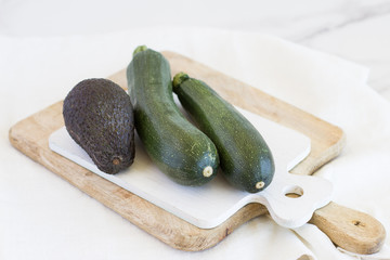 un aguacate y dos calabacines enteros sobre tablas de cortar de madera